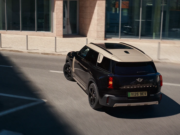 מבט אחורי מלמעלה של ה-MINI Countryman החשמלית בצבע שחור Midnight Black וגג בצבע כסף Vibrant Silver בחניה,